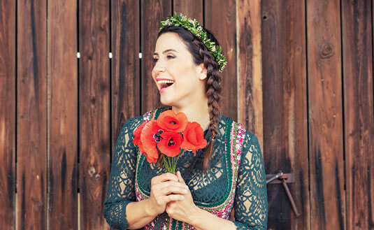 Frau mit braunen Haaren, geflochtenem Zopf, Dirndl und Blumenstrauß lacht