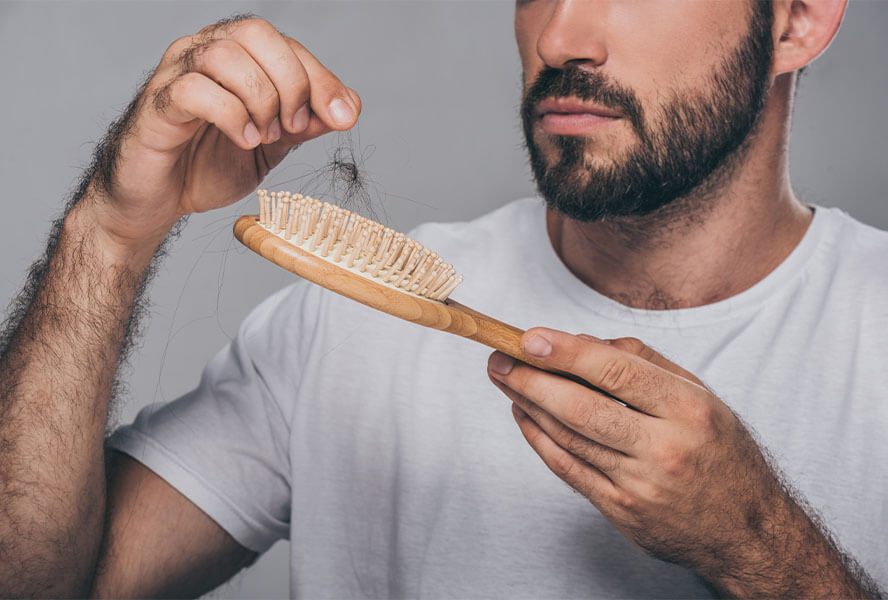 Mann mit dunklem Bart hält Bürste mit Haaren in der Hand