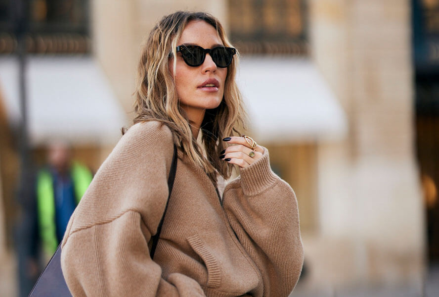 Frau mit dem Trend-Haarschnitt Mermaid Cut und leichten Wellen und Balayage trägt eine Oversize Wolljacke in Camel