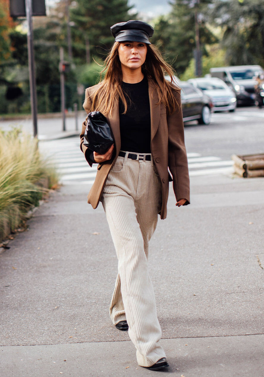 Frau mit einer Mütze trägt ein Blazer Outfit bestehend aus braunem Blazer, weisser Hose und schwarzem Top