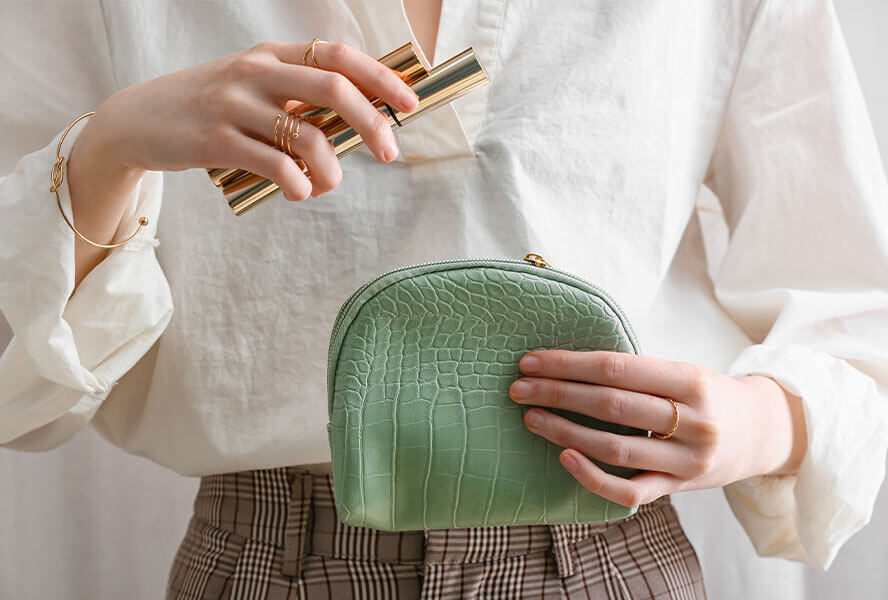 Frau hält ihre grüne Kosmetiktasche und Mascara in der Hand