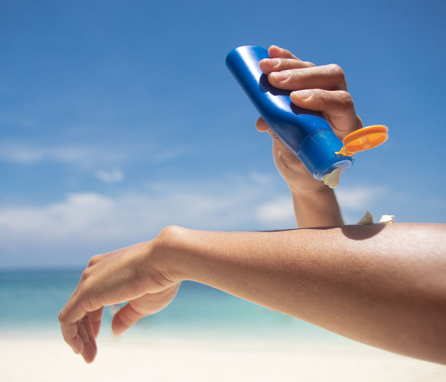 Frau mit langen, braunen Haaren und Sonnenhut am Strand