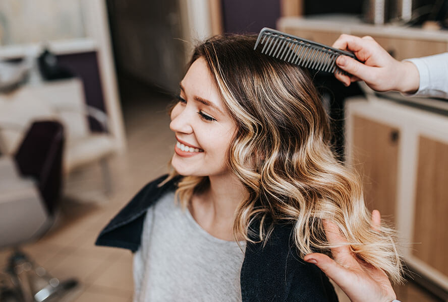 Frau mit Balayage Strähnen sitzt beim Friseur und wird beraten