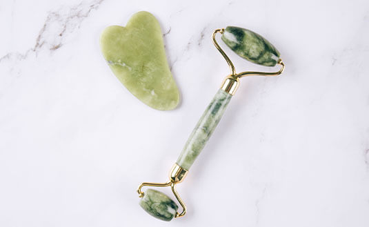 Gua Sha aus grüner Jade auf Marmor-Untergrund