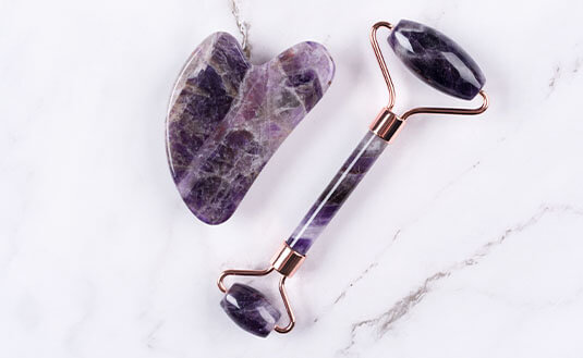 Gua Sha aus lilafarbenem Amethyst auf Marmor-Untergrund