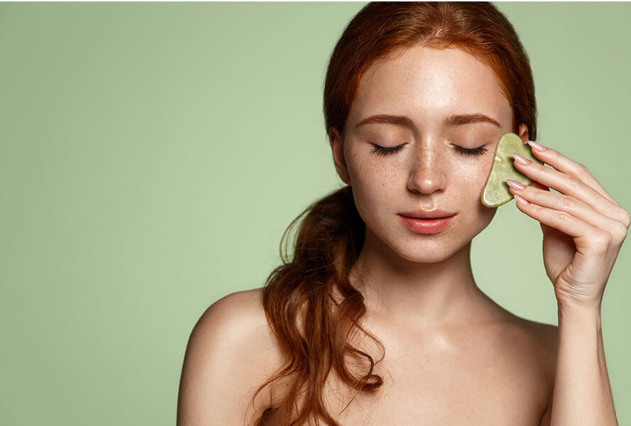 Frau mit einem Gua Sha Stein in der Hand und ihr Gesicht mit einer Lymphdrainage pflegt