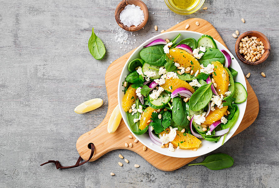 Salatschüssel auf Holzbrett mit Salz, Zitronen und Pinienkernen