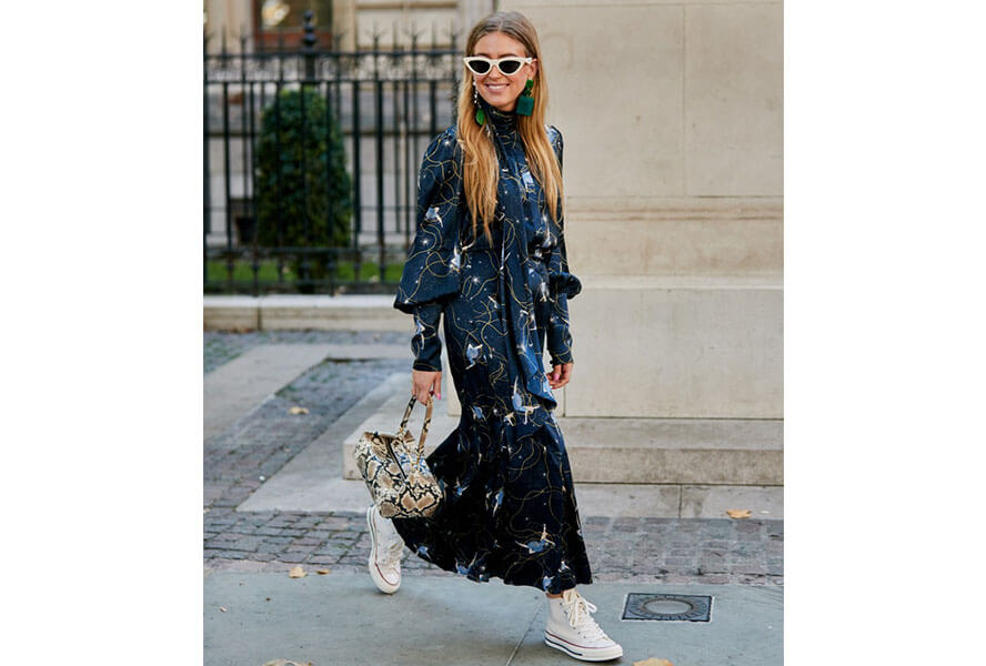 Blonde Frau mit weisser Sonnenbrille und blauem Maxikleid trägt weiße Stoffsneaker