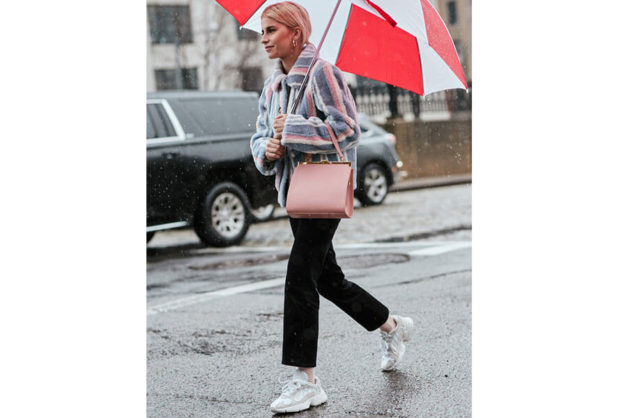 Caro Daur mit kurzem Mantel und einem Regenschirm trägt weisse Retro Sneaker